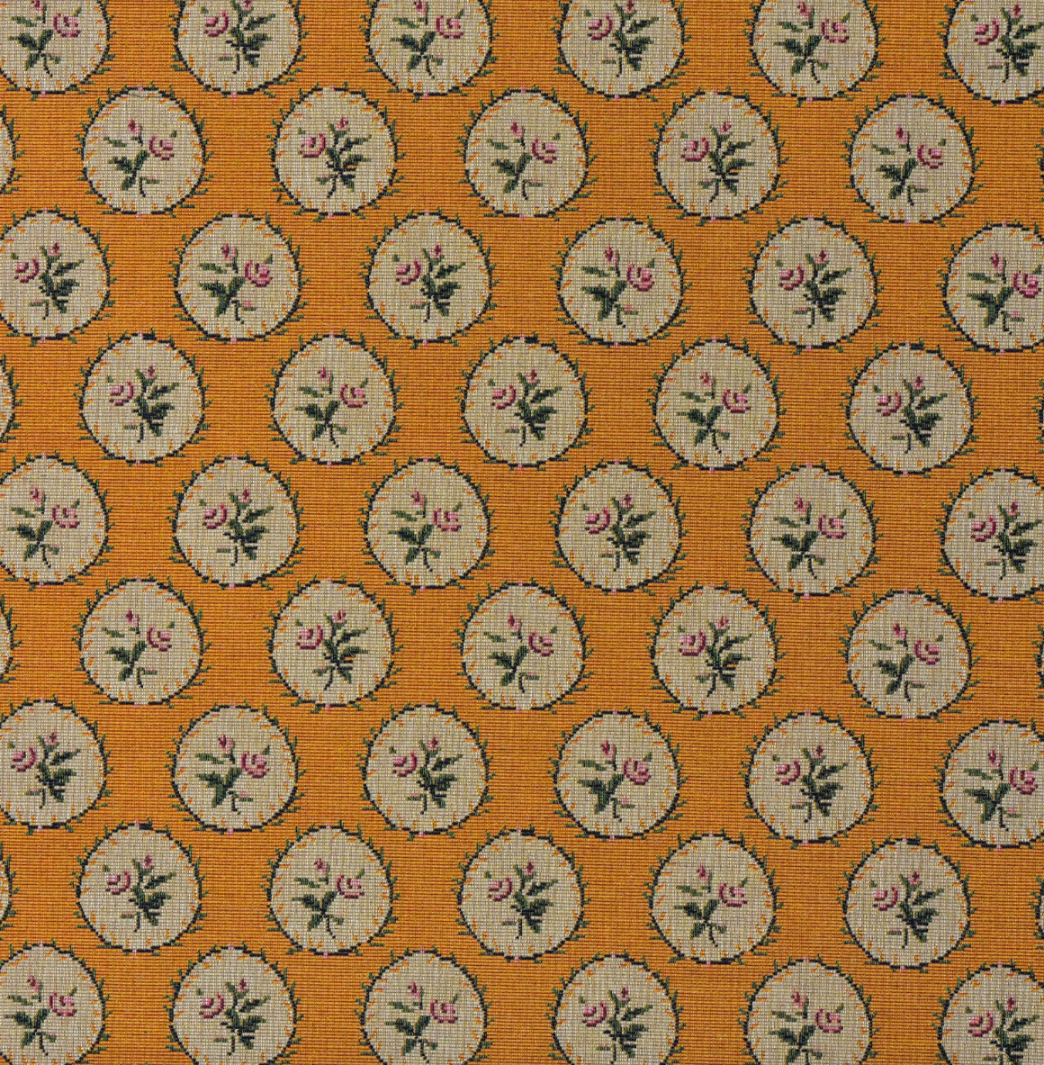 A close-up of a woven fabric pattern featuring a repeating circular motif with pink flowers and green leaves on a warm orange background.