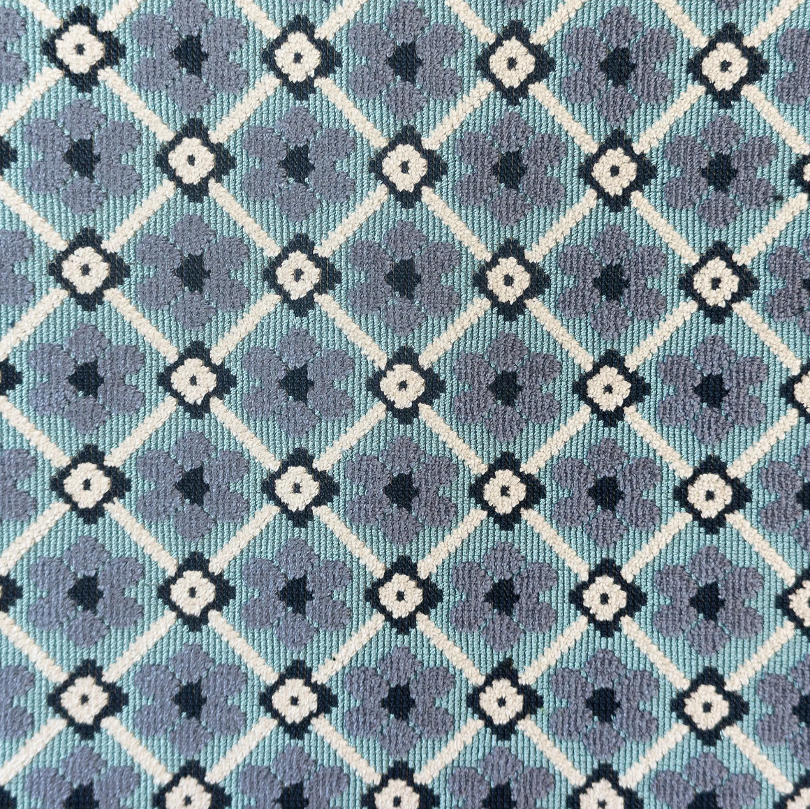 A close-up of a woven fabric with a repeating geometric pattern of white and dark gray floral motifs inside olive green diamonds.